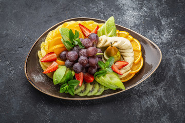 Raw fruits berries platter, oranges, kiwi strawberries,  grapefruit grapes, bananas apples on the plate, dark background