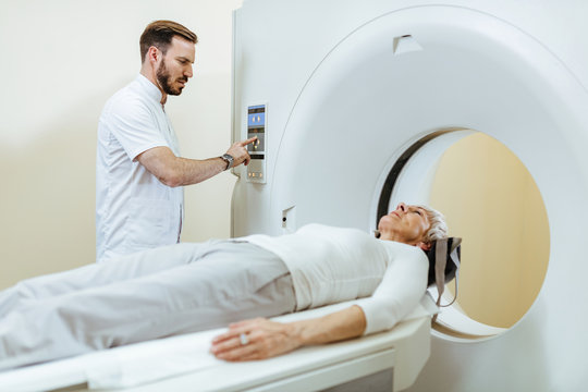 Medical technician starting MRI scan procedure of mature patient in examination room.
