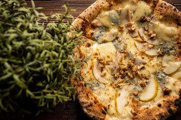 Pizza z gruszką, orzechami i kozim serem na drewnianym, naturalnym, brązowym stole. Obok rozmaryn...