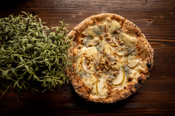 Pizza z gruszką, orzechami i kozim serem na drewnianym, naturalnym, brązowym stole. Obok rozmaryn w doniczce - obrazy, fototapety, plakaty