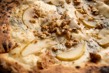 Pizza z gruszką, orzechami i kozim serem na drewnianym, naturalnym, brązowym stole. Obok rozmaryn w doniczce