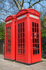 Fototapeta premium Pair of old-fashioned red British phone boxes standing on a spring sidewalk in London, UK