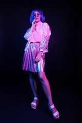 Fashionable young woman in neon light in full growth in a nightclub. The girl is wearing a wig,...
