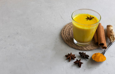 Alternative medicine, Indian drink golden milk or latte with turmeric, Turmeric powder, turmeric root, cinnamon, ginger, badian on a gray background