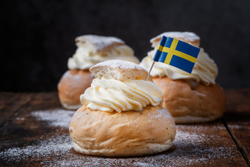 Traditional Scandinavian cream and almond paste filled cardamom bun Semlor with a Swedish flag.