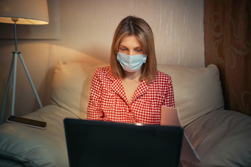 Young businesswoman in a medical protective mask works from home at the computer during self-isolation and quarantine. Virus coronavirus outbreak, flu epidemic and covid ncov novel. Stay home.