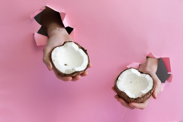 Two male hands hold two halves of coconut through holes in a paper wall