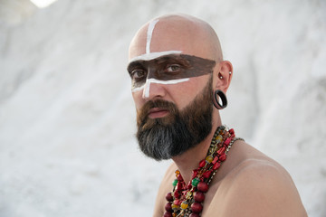 young man with primal makeup and beads spells with powder in hands on white rocks
