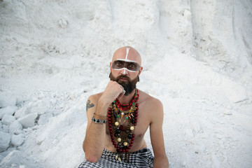young man with primal makeup and beads spells with powder in hands on white rocks