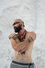 young man with primal makeup and beads spells with powder in hands on white rocks