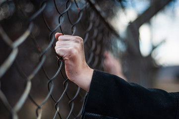 The migrant is holding his hands behind the protective fence
