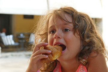 Pretty little girl with big eyes eats a croissant for breakfast