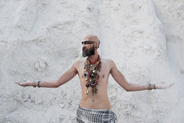 young man with primal makeup and beads spells with powder in hands on white rocks