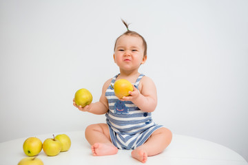 Fototapeta na wymiar Happy toddler sits and eats apples on a white background