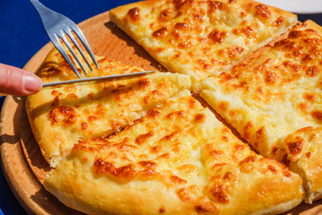 Cutting Four cheese pizza quattro fromaggi with knife on a wooden board, blue background