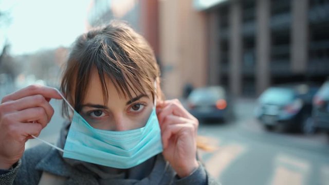 Coronavirus pandemic. Close-up portrait woman wearing medical face mask, looking to camera on urban background. Prevention of bacterial infection, Corona virus, Covid 19. - Powered by Adobe