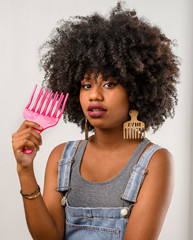  jovem mulher com cabelo estilo afro segurando um pente garfo demonstrando o cuidado com o cabelo...