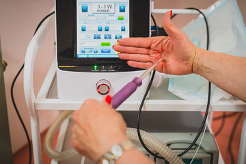 Female doctor is holding a laser used for vaginal treatment of incontinence, Visible ray of laser beam in a hand shaped as a vaginal entrance. Laser control screen seen in the background.