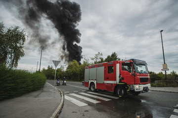 Fototapeta na wymiar Photo of a fire next to a motorway in Stegne, Ljubljana, Slovenia. Dark plume of smoke is visble rising up from the place of ignition with red fire truck seen in the foreground.