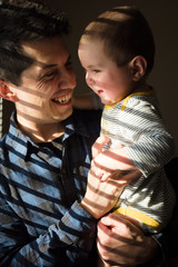 Father holding baby and smiling at home