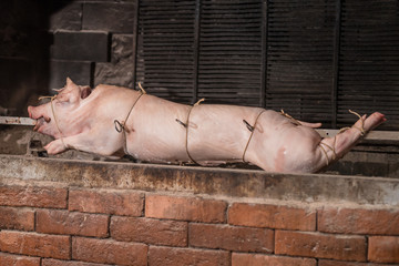 Pig on a metal rod is being prepared to be turned on a traditional balkan grill called rostilj or odojek. Fresh pig waiting on a grill.