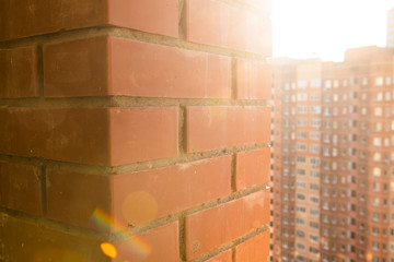Thick brick wall against high-rise building and sun rays on the background