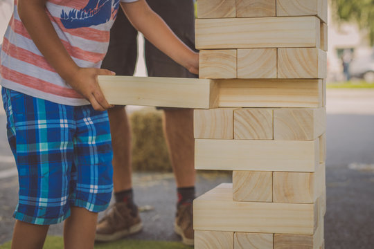 Kid playing  maxi jenga game a game where big wooden blocks are removed from a wooden tower. Focus on kids hands removing a block.