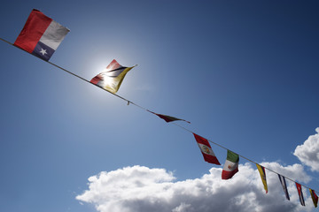 Flags of the world flutter in the breeze set agains a blue sky and fluffy white clouds