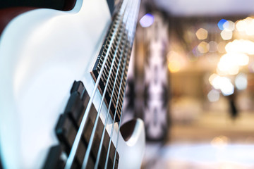 A white electric bass guitar with five strings close-up. Blurred background.