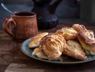 Ceramic folk cup of coffee with milk, home-made cheesecakes in a plate on a wooden table in the kitchen.