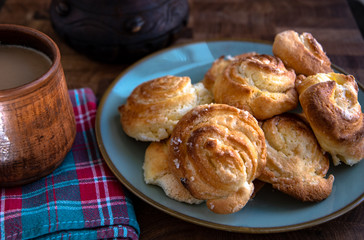 Ceramic folk cup of coffee with milk, home-made cheesecakes in a plate on a wooden table in the kitchen.