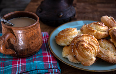 Ceramic folk cup of coffee with milk, home-made cheesecakes in a plate on a wooden table in the kitchen.
