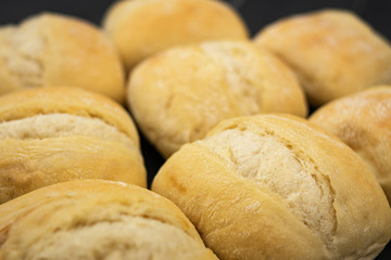 Heap of freshly baked and golden bread ready for consumption on gray wooden table with light traces of flour