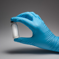 Hand in glove with a vaccine vial against the virus on a gray background. White powder inside an...