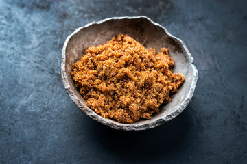 Traditional brown muscovado sugar offered as closeup in a rustic earthenware dish with copy space