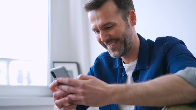 Happy man at home using smartphone