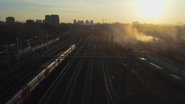 View from a drone on a train moving through the industrial zone, on a multi-track railway in the rays of the setting sun.