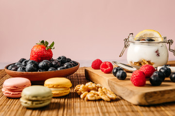 top view of a snack consisting of blueberries, raspberry, yogurt and macarons, on a background of wooden sticks
