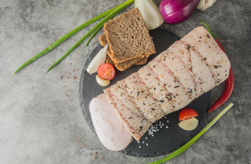 A large piece of white lard with spices covered in twine on a black slate with bread and...
