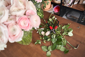 The leaves and cutting the stems and pruning shears on the table, the workflow. Floral shop concept . Florist woman creates flower arrangement in a wicker basket.