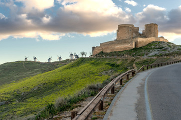 View of the medieval castle of Consuegra (Spain) next to a group of ancient windmills, on the route of the Don Quixote and Cervantes mills, at sunset.