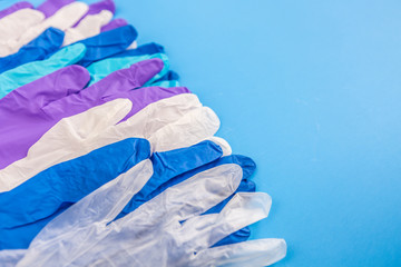 Flat lay composition with different medical multicolor gloves in a row on blue color background. Space for text