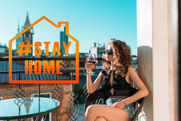 Pretty european girl in a black bodysuit with a glass of wine sits on a balcony against the...