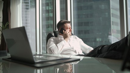 A man in a white shirt has put his feet on the desk. Businessman in white shirt put legs on desk