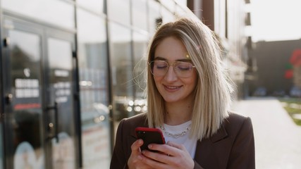 beautiful young caucasian woman in sunlight using phone in the city center, smiling. Internet, business, outside, technology, eye, spring, mobile, portrait. Close up