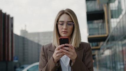 Portrait pretty young businesswoman using smartphone at street Serious woman typing message on smartphone outdoor. European girl holding mobile phone in hand outdoor. Business woman chatting online