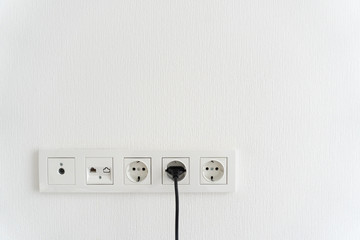 black cable cord pluged in receptacle of modern electric socket in multi paneling, internet, tv or...