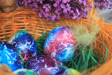 Easter background. Art decorated eggs with lilac and feather in basket.