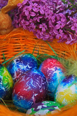 Easter background. Art decorated eggs with lilac and feather in basket.