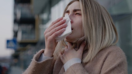 Sad young woman sneezing coughs feel sick at outdoor fever cold allergy disease female nose sneeze...